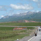 The peloton at the Tour of Qinghai Lake through the mountainous landscape at around 3000 meters altitude, with peaks over 4000 meters surrounding. (photo: Remko Kramer)