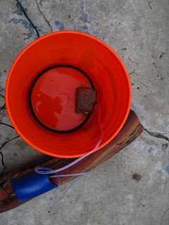The soaker hose ring inside the bucket. Anchored by a brick. Duct tape would work just as well.
