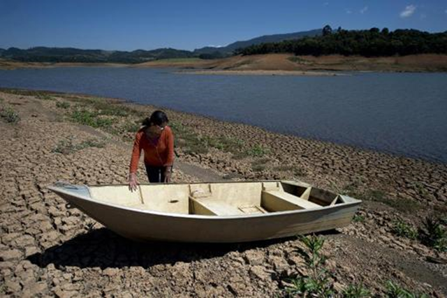 A local resident stands next to a boat near the bank of Jacarei river dam, in Piracaia, as a record drought affects Sao Paulo state in Brazil, on 19 November 2014. Photo: Nelson Almeida