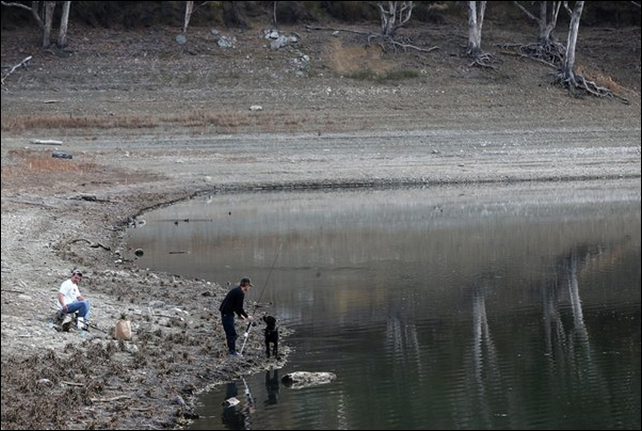Two fishermen and their dog try to catch fish at a record-low California reservoir. California wildlife officials have banned fishing in several rivers to protect salmon and steelhead trout during a severe drought that follows the state's driest year on record. California is in its third straight year of drought conditions. Reservoirs throughout the state have low water levels. 28 January 2014 Photo: Justin Sullivan / Getty Images
