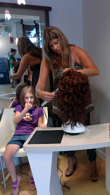 Sonja styles the wig and Emma touches her nose?