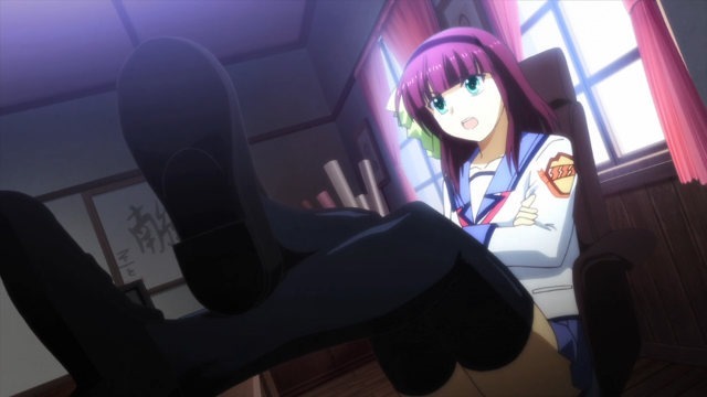 An angled shot from the feet of a girl leaning back in a chair with her legs propped on a desk, arms crossed
