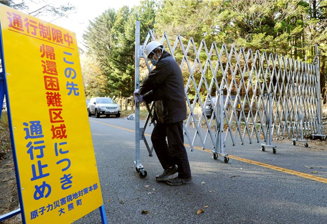 An official closes a barrier at an access point to the 'Difficult-to-return zone' in Okuma, Fukushima Prefecture. Photo: Asahi Shimbun