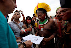 Legendary Chief Raoni receives a banner sketch from artist John Quigley before nearly 1500 people used Rio’s Flamengo Beach as a canvas on June 19, 2012. Their bodies formed the lines of an enormous image promoting the importance of free-running rivers, truly clean energy sources like solar power and including indigenous knowledge as part of the solution to climate issues. The activity was led by Brazil’s many indigenous peoples organized under the umbrella of the Articulation of Brazilian Indigenous Peoples. ©Caroline Bennett