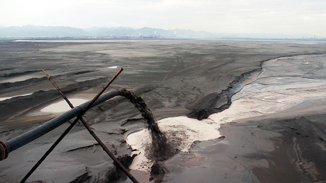 Hidden in an unknown corner of Inner Mongolia is a toxic, nightmarish lake created by our thirst for smartphones, consumer gadgets and green tech, discovers Tim Maughan. Black sludge pours into the lake - one of many pipes lining the shore. Photo: Liam Young / Unknown Fields