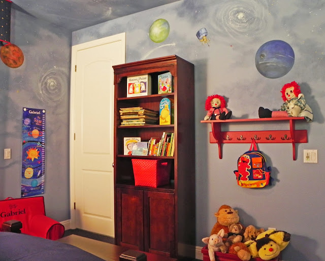 A bookcase holds favorite books and treasures. A shelf with hooks below holds his backpack and other toys.
