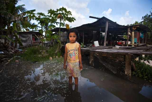 Teuga Patolo stands in king-tide waters that surround her neighbour's house on Kiribati. A three-year study by Australia's CSIRO and Bureau of Meteorology suggests the Pacific's small island states can expect rising sea levels, more heavy rainfall events, more very hot days and more cyclones. Rodney Dekker / Oxfam