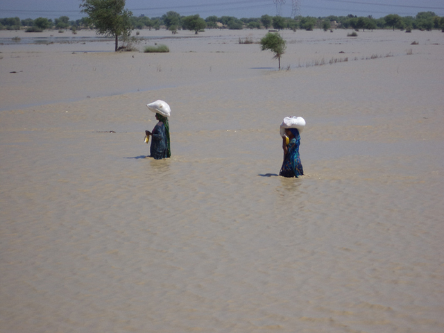 Two Pakistani women carry loads while wading through floodwaters, 13 September 2012. muslimhandsuk / flickr