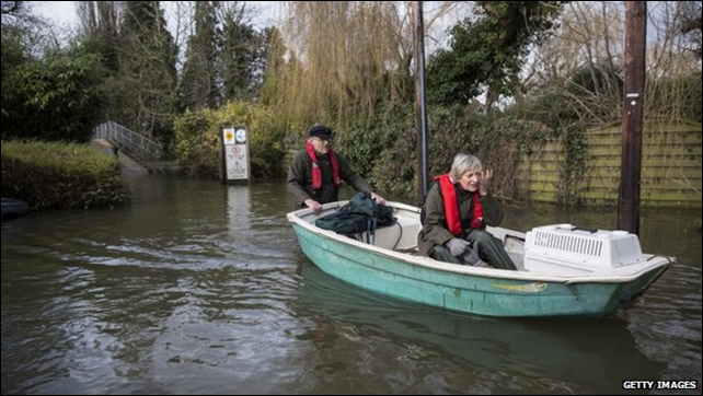 An man pushes a boat carrying his wife and their pet through floodwaters in Britain, 12 February 2014. The swollen River Thames caused major flooding after the UK's wettest January since 1766. Photo: Getty Images / BBC News