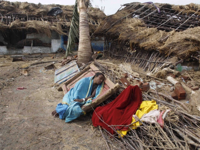 An Indian woman rests near her damaged house after returning to the cyclone hit Podampeta village on the Bay of Bengal coast in Ganjam district, Orissa state, India on 13 October 2013.  The strongest cyclone to hit India in more than a decade  made landfall in eastern Orissa state, officials said they only knew of 17 fatalities, most of them people killed by falling branches or collapsing buildings in the rains ahead of the cyclone. Photo: Biswaranjan Rout / The Associated Press