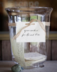 A large hurricane vase is displayed with stacks of rubber-stamped cards for guests to write on. Stones from a nearby beach weigh down the cards. A large hurricane vase is displayed with stacks of rubber-stamped cards for guests to write on. Stones from a nearby beach weigh down the cards.