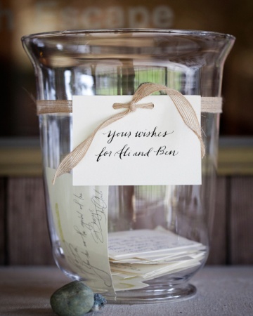 A large hurricane vase is displayed with stacks of rubber-stamped cards for guests to write on. Stones from a nearby beach weigh down the cards. A large hurricane vase is displayed with stacks of rubber-stamped cards for guests to write on. Stones from a nearby beach weigh down the cards.