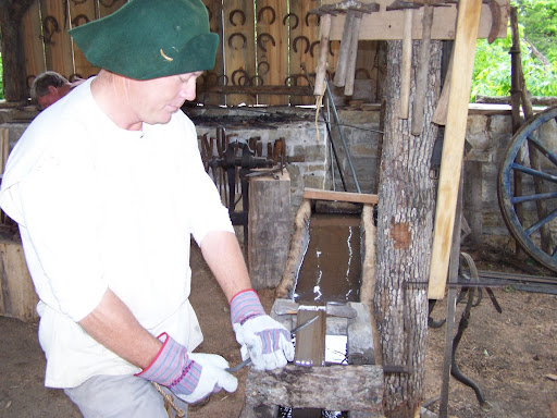 Rocky Horton demonstrates how a primitive blacksmith tool smooths a nail.  He’s powering the wheel with a pedal that he’s pumping with his foot.