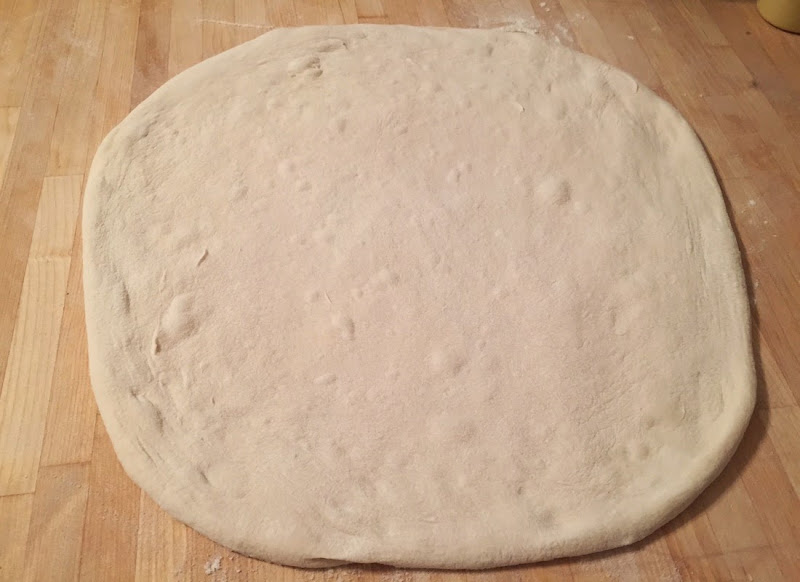 Pizza dough shapped in a roughly circular form.