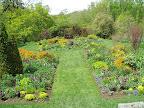 The tennis court garden viewed from the house: you can see the formal lines, focal point, and abundant plantings that make this such a beloved garden style.