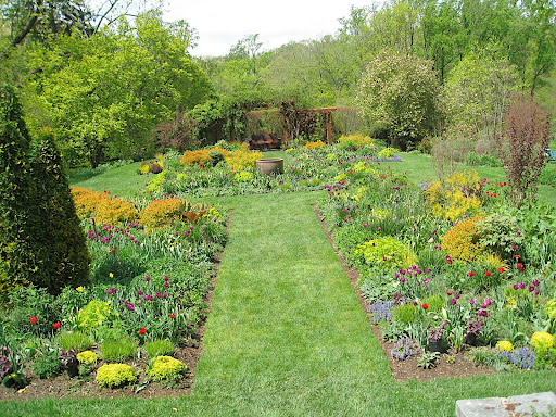 The tennis court garden viewed from the house: you can see the formal lines, focal point, and abundant plantings that make this such a beloved garden style.
