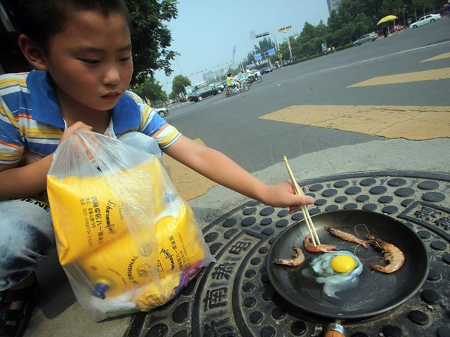 A child cooks shrimp and an egg in a frying pan heated by a manhole cover on a hot summer day on 31 July 2013 in Jinan, China. It has been so hot that eggs are hatching without incubators and a highway billboard burst into flames in the worst heat wave in at least 140 years. Photo: China Daily / AP