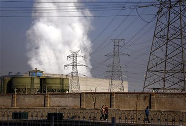 Pedestrians walk along a footpath in front of a massive chimney billowing smoke for a coal-burning power station in central Beijing, 12 January 2012. David Gray / Reuters