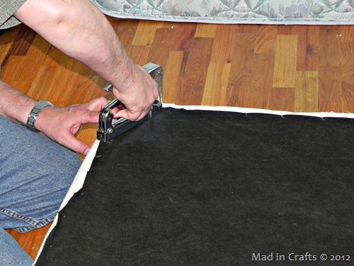 hands using a staple gun to reapply the underside of the box spring
