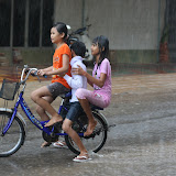 Three kids on a bike in a torrential rainstorm.