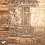 Shown, in central panel, a semi-god with four hands. In above two hands, he is holding something, snake? while lower one hands is in varada pose. There is a vessel on the ground, near his feet. Any suggestions???