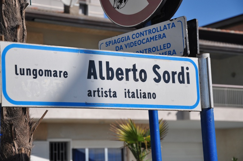 un cartello stradale "lungomare Alberto Sordi (artista italiano)"