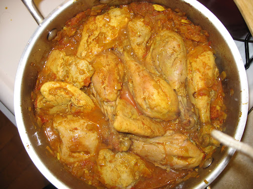 The roasted chicken is added to a skillet with spices, onion, tomatoes, ginger, garlic, and the reserved marinade.