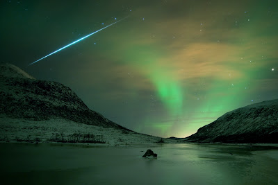 The Northern lights shimmer gently over the wintry coast of Tromsø Norway, contrasted with the streak of a meteor from the Geminid meteor shower