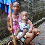  &ndash; Lucy Mansaray, age 11, pounding cassava and caring for her little brother, "Roo". (©NHA photo James Mansaray 7 June 2007)