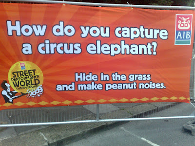 Sign from the Street Performance World Championships reading How do you campture an Elephant? Hide in the grass and make elephant noises-