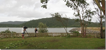 News crews report on the damage at Airlie Beach with a sailboat devastated on the rocks behind them (click to enlarge)