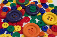 Various blue, red, green yellow and orange buttons spilled on a white posterboard