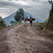 Youth pushing a bike with logs up a muddy road near volcano