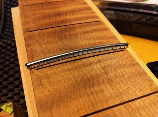Note that the fret slots do not extend all the way to the edges of the fretboard! This board was radiused (16" to 20" compound radius) and slotted on a CNC for hyper-accurate fret placement. Stopping the fret slots short of the edges of the board gives a "bound" look without binding, and makes the board stiffer overall, since it has 3 mm "rails" down each side. Normally a slotted board wants to curl up, since you're essentially cutting kerfs into the piece of wood. The slots themselves are also radiused to match the board, so there's no waste of material there either.