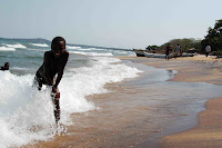 Boys in the waves at Senga Bay I took this picture at Senga Bay on Lake Malawi. This lake is huge - you can only see the other side (the mountains of Mozambique) on a very clear day. It took me two days to figure out why, other than missing the smell of salt in the air, this place feels different and somehow safer than a real ocean. Finally I realized it was the cadence of the waves. They are driven by strong winds rather than the rotation of the earth so they come in faster and on most days, weaker. In general Malawian kids love having their pictures taken. This little boy in briefs was obviously no exception. In the background you can see a large drift boat as well as several hand-made dug out canoes. When I was there the fishermen had to go out at night because the wind and waves were too great during the day. The canoes and drift boats were still navigating back to shore by kerosene lantern light until three o'clock that morning.