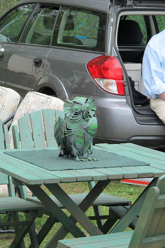 The green owl on the wooden deck set seems as if it were arranged already on someone's porch.