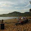 Sitting at a table on the beach, looking right.