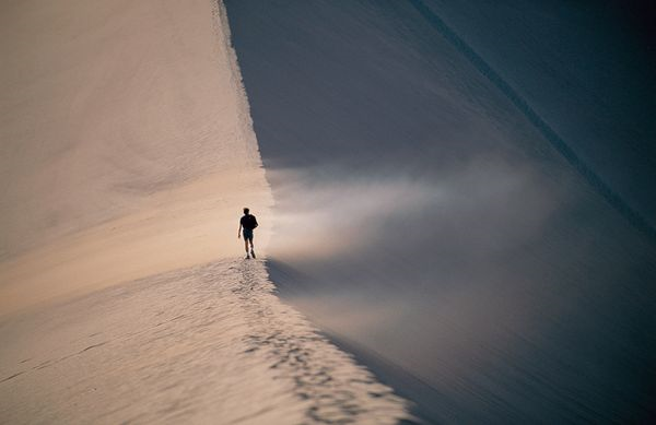 A person walks into the path of blowing sand on the crest of a dune in Chile's Atacama Desert. Photograph by Joel Sartore, National Geographic