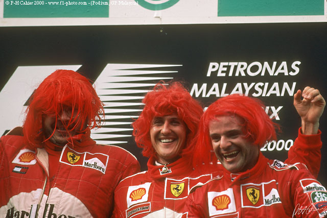 Росс Браун, Михаэль Шумахер и Рубенс Баррикелло в красных париках на подиуме Гран-при Малайзии 2000