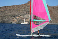 Damien sur la planche en 1 plan, le bateau en 2 et une falaise en 3 plan.
