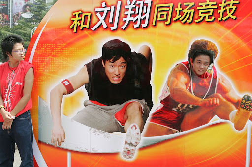 SHANGHAI, CHINA - SEPTEMBER 16: (CHINA OUT) A Chinese man poses for pictures with a billboard featuring Olympic 110-meter hurdles champion Liu Xiang at Shanghai Stadium, where the Golden Grand Prix will be held, on September 16, 2005 in Shanghai, China. The 2005 Shanghai Golden Grand Prix will begin on September 17. (Photo by China Photos/Getty Images)