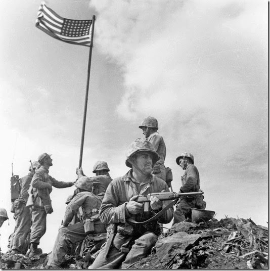 This is the first flag raising on the top of Mt. Suribachi. The famous flag-raising photo was taken when the second flag was put up later that day. This photo was taken by Leatherneck's Lou Lowery.