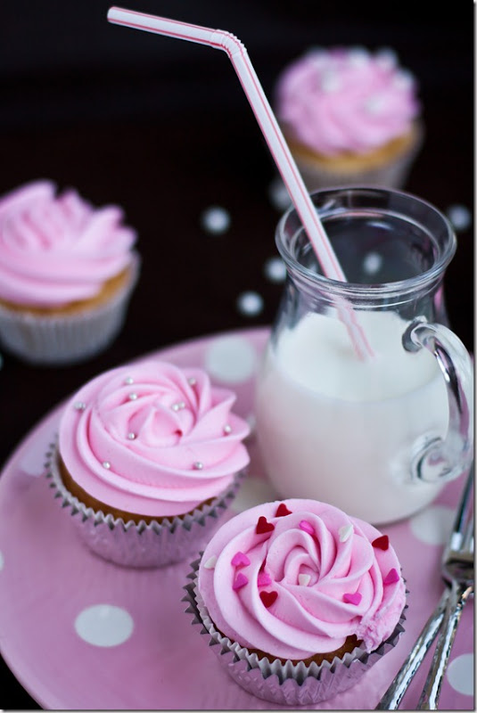 Two vanilla cupcakes on a pink plate with a pitcher of milk. 