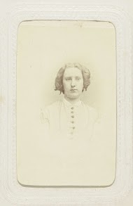 Studioportret van een vrouw in een hooggesloten jurk en pijpenkrullen in het haar