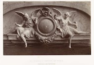 Twee beelden van vrouwelijk engelen met slaghamers in de hand, zittend aan weerszijden van een medaillon, gesitueerd boven een deurpartij.