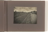 Auto op onverharde weg, op de bumper zit een man