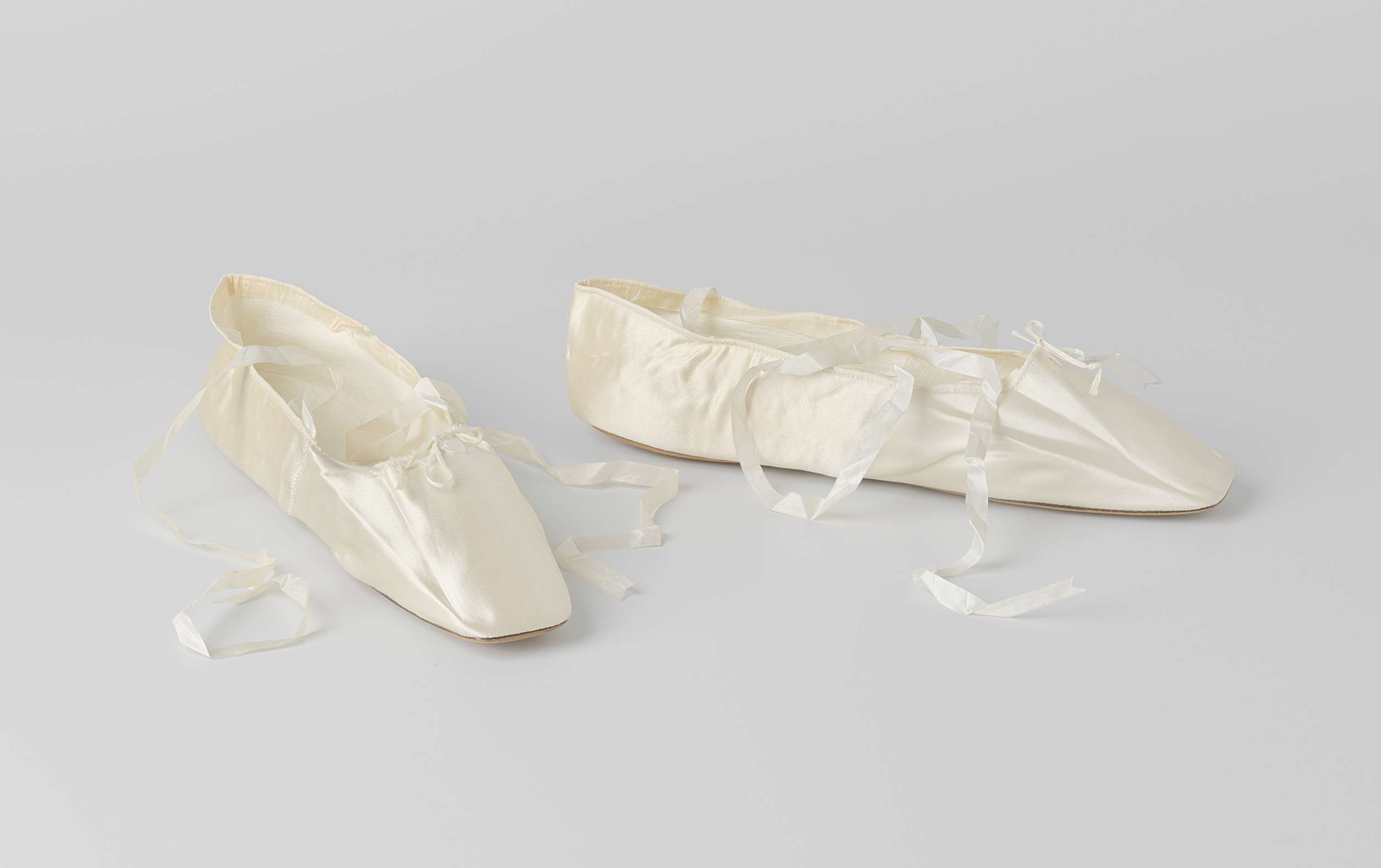 Bruidsschoen plat model met enkelband en dunne witte zijden linten van crème satijn, versierd met een kleine witte satijnen strik