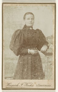 Studioportret van een jongevrouw met oorbellen in hooggesloten zwarte jurk met pofmouwen