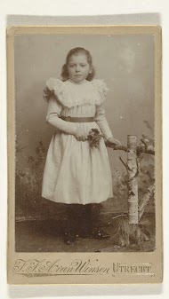 Studioportret van een meisje bij een hek met bloemetjes in haar hand