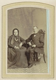 Portret van een vrouw in een jurk met hoofddeksel en een zittende man